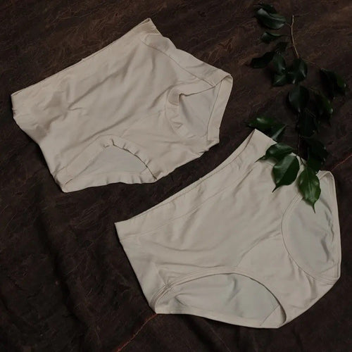 Two pairs of undyed mugwort underwear laid flat with green leaves, gusset visible